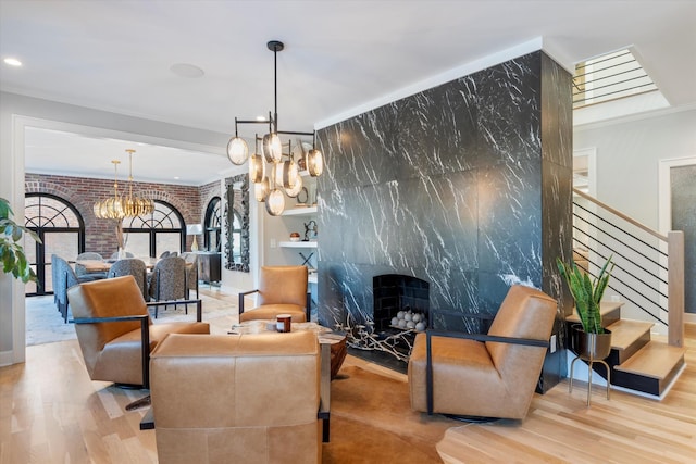 community lobby with a premium fireplace, brick wall, light wood-type flooring, and a chandelier