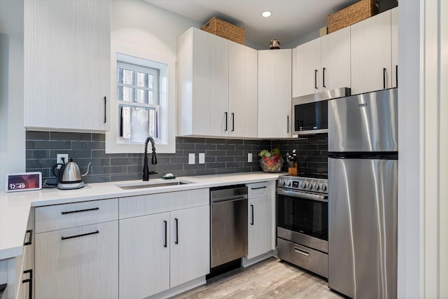 kitchen with appliances with stainless steel finishes, light hardwood / wood-style floors, sink, and backsplash