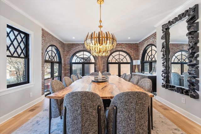 dining space with an inviting chandelier, light wood-type flooring, ornamental molding, and brick wall