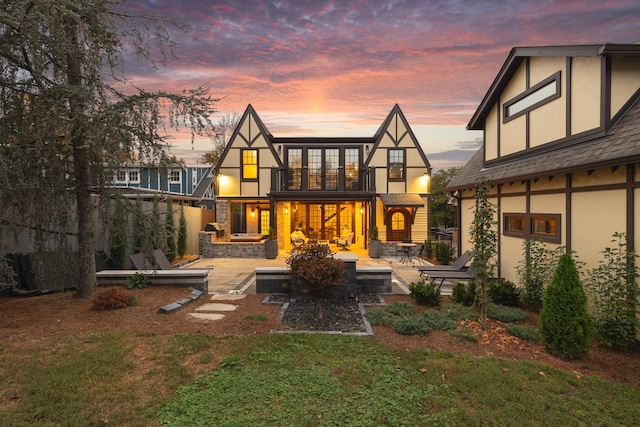 back house at dusk with a yard, a patio, and a balcony