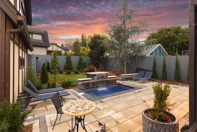 pool at dusk featuring a hot tub, a patio, and pool water feature