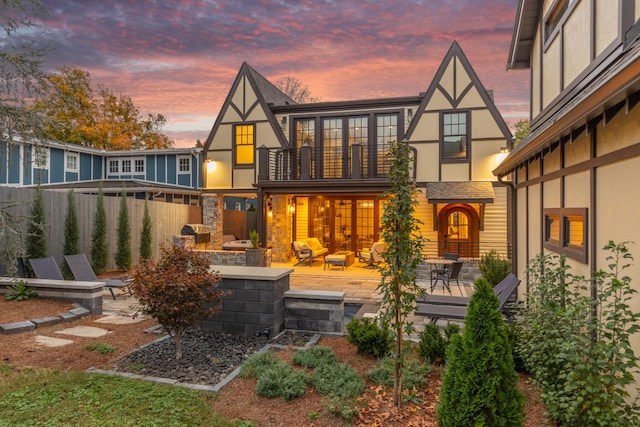 back house at dusk with a patio, a balcony, and an outdoor living space with a fire pit