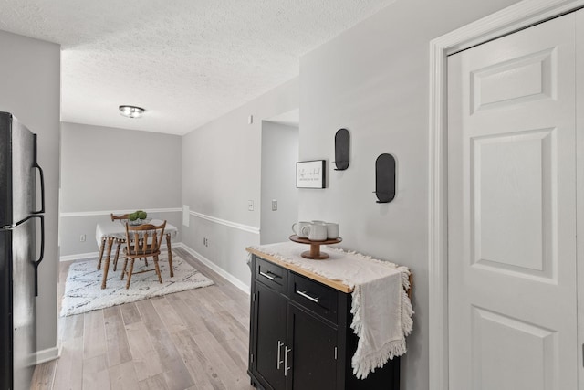 kitchen featuring black refrigerator, a textured ceiling, and light wood-type flooring