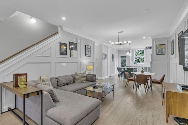 living room featuring a notable chandelier, ornamental molding, and light wood-type flooring