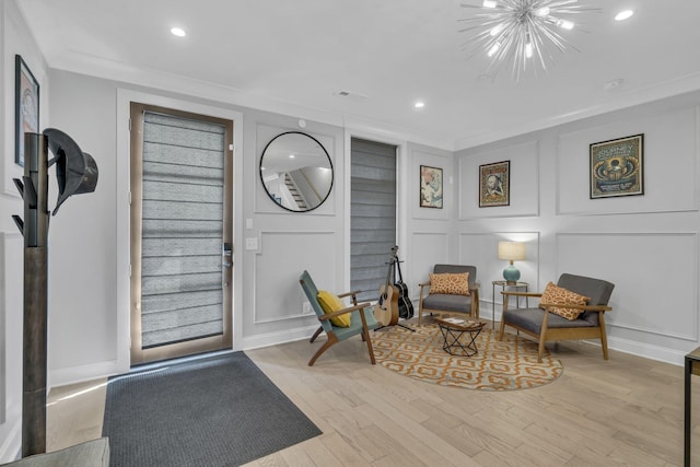 living area with crown molding, a chandelier, and light hardwood / wood-style floors