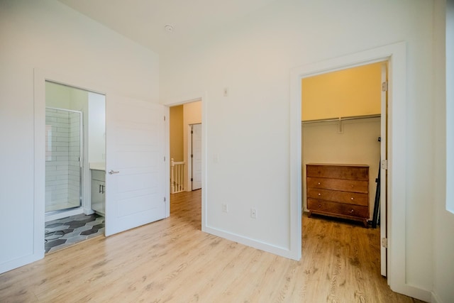 unfurnished bedroom with a spacious closet, light hardwood / wood-style flooring, ensuite bath, and a closet