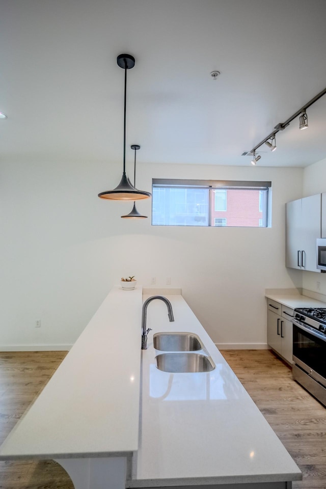 kitchen featuring appliances with stainless steel finishes, white cabinetry, sink, hanging light fixtures, and light hardwood / wood-style floors