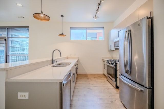 kitchen with pendant lighting, sink, appliances with stainless steel finishes, a healthy amount of sunlight, and kitchen peninsula