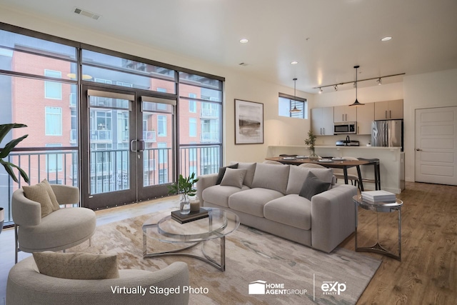 living room featuring rail lighting, light hardwood / wood-style flooring, and french doors