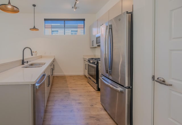 kitchen with light countertops, rail lighting, light wood-type flooring, a sink, and appliances with stainless steel finishes