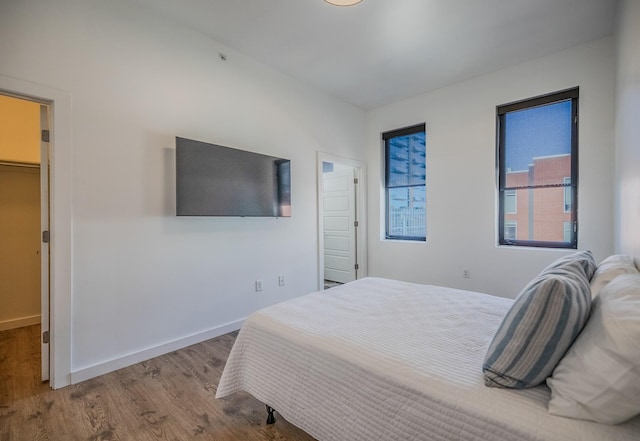 bedroom featuring baseboards, wood finished floors, and a spacious closet