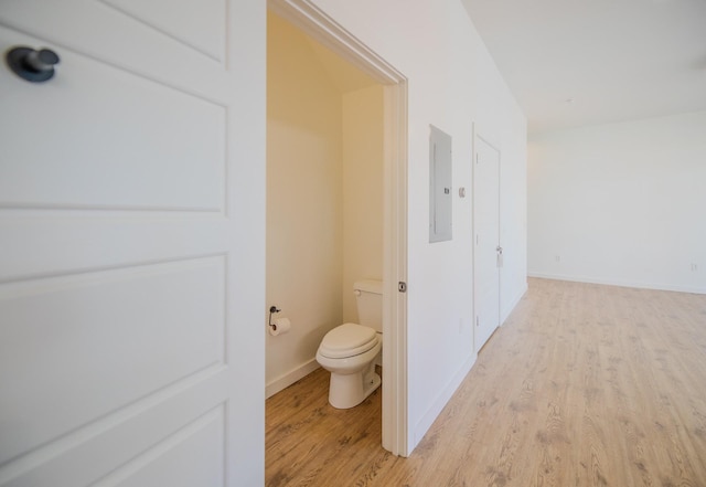 bathroom with baseboards, wood finished floors, toilet, and electric panel