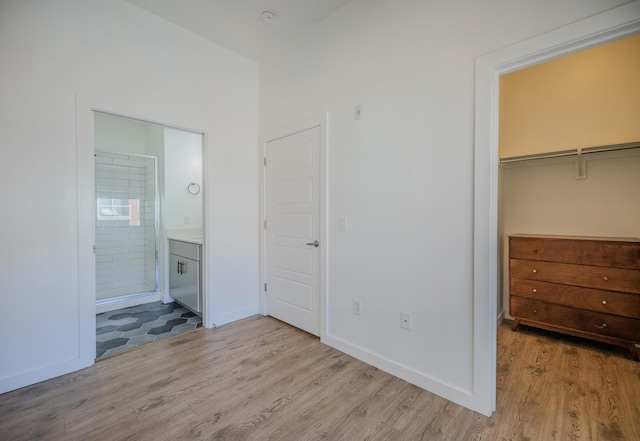 unfurnished bedroom featuring a closet, a spacious closet, baseboards, ensuite bathroom, and wood finished floors