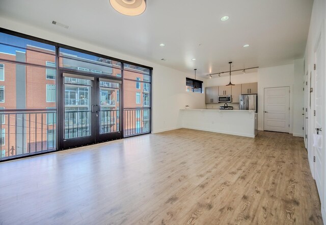 unfurnished living room featuring rail lighting, a wall of windows, french doors, baseboards, and light wood-style flooring