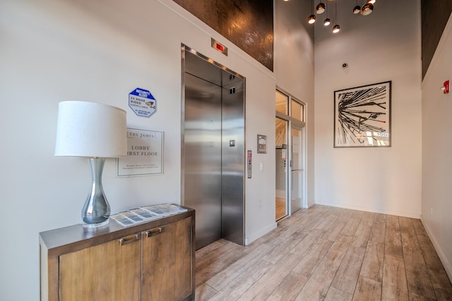 hall featuring elevator, baseboards, and light wood-type flooring