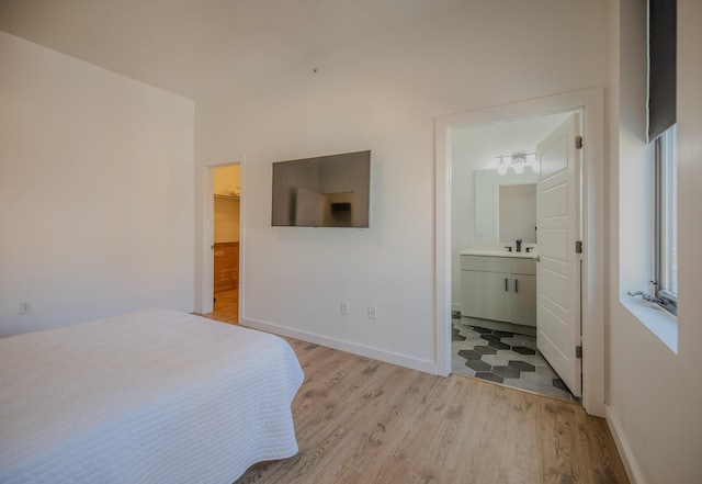 bedroom with light wood finished floors, baseboards, a walk in closet, and a sink