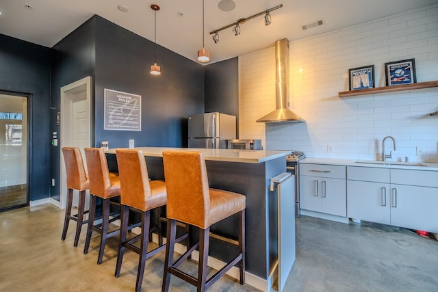 kitchen with light countertops, concrete flooring, a sink, appliances with stainless steel finishes, and wall chimney exhaust hood