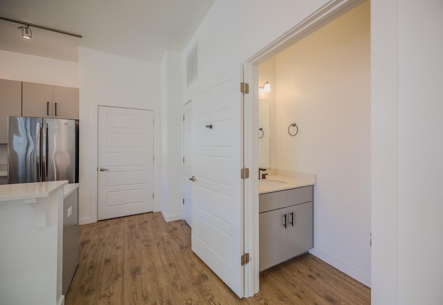 hall with light wood-style flooring, a sink, and baseboards