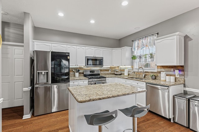 kitchen with a kitchen island, hardwood / wood-style floors, sink, white cabinets, and stainless steel appliances