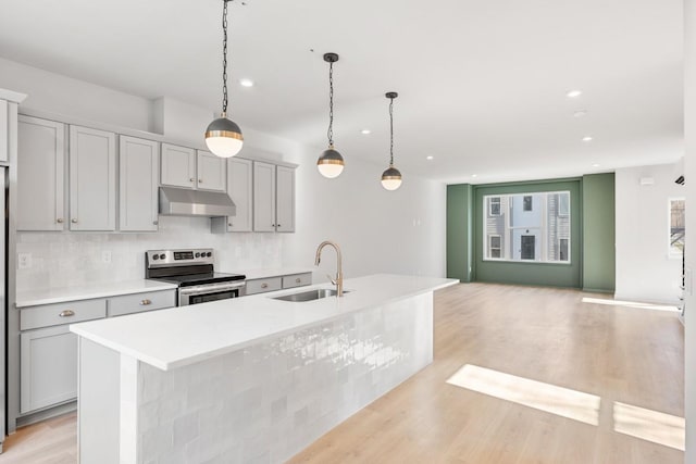 kitchen featuring stainless steel range with electric stovetop, sink, gray cabinetry, and an island with sink