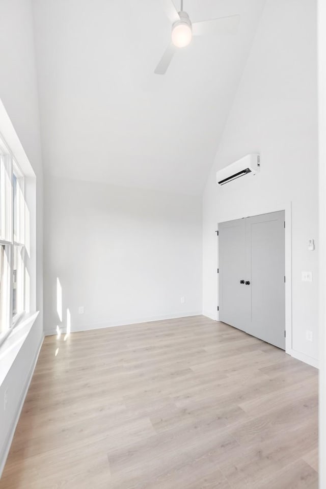 unfurnished room featuring high vaulted ceiling, a wall mounted AC, ceiling fan, and light hardwood / wood-style flooring