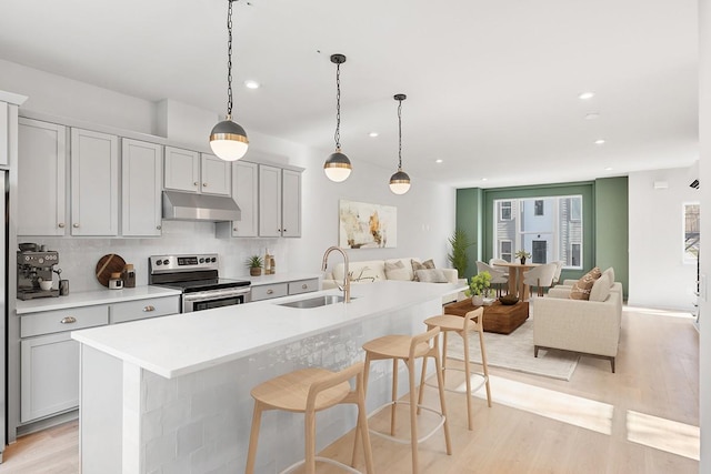 kitchen with sink, a kitchen island with sink, stainless steel electric stove, and decorative light fixtures