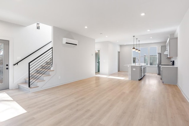 unfurnished living room with a wall mounted AC, sink, and light hardwood / wood-style flooring