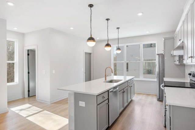 kitchen featuring an island with sink, light wood-type flooring, stainless steel appliances, decorative light fixtures, and sink