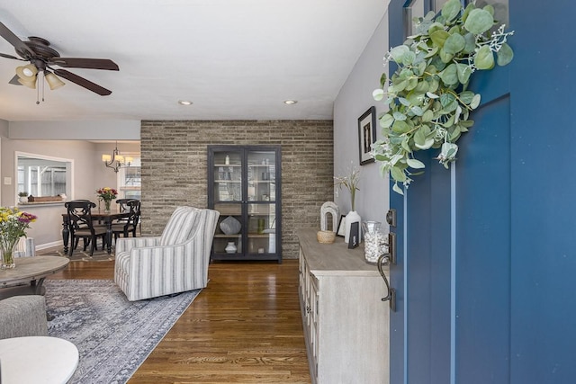 living room with dark wood-type flooring, brick wall, and ceiling fan with notable chandelier