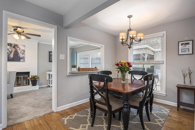 dining space featuring dark hardwood / wood-style flooring, ceiling fan with notable chandelier, a fireplace, and ornamental molding