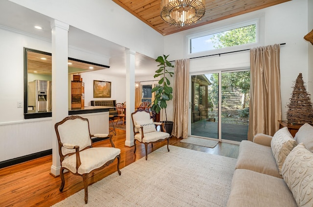 living area featuring decorative columns, crown molding, wooden ceiling, and light wood-type flooring