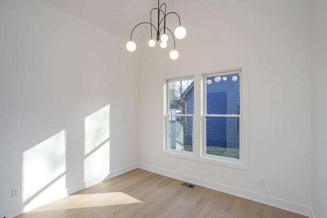 spare room featuring an inviting chandelier and light wood-type flooring