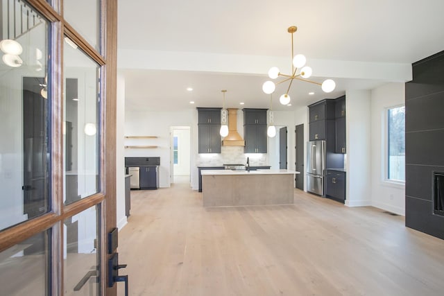 kitchen with light hardwood / wood-style flooring, a kitchen island with sink, high quality fridge, decorative backsplash, and decorative light fixtures