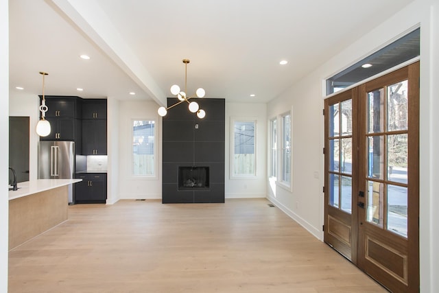 unfurnished living room with french doors, sink, light hardwood / wood-style flooring, a tile fireplace, and a notable chandelier