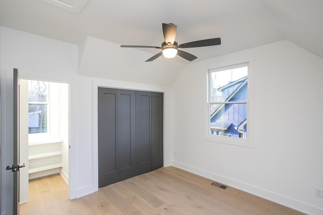 unfurnished bedroom featuring light wood finished floors, multiple windows, visible vents, and vaulted ceiling