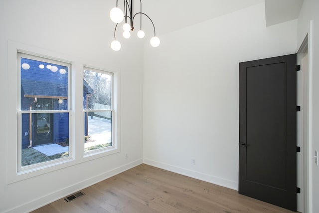 empty room featuring a healthy amount of sunlight, a chandelier, and light hardwood / wood-style flooring