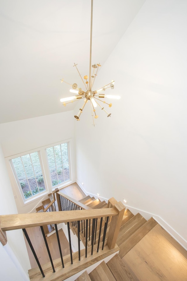 stairway with an inviting chandelier, hardwood / wood-style flooring, and a high ceiling