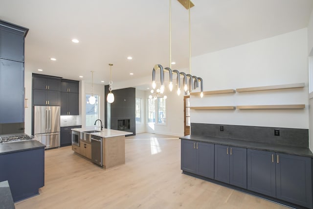 kitchen with light hardwood / wood-style flooring, stainless steel appliances, a fireplace, an island with sink, and decorative light fixtures