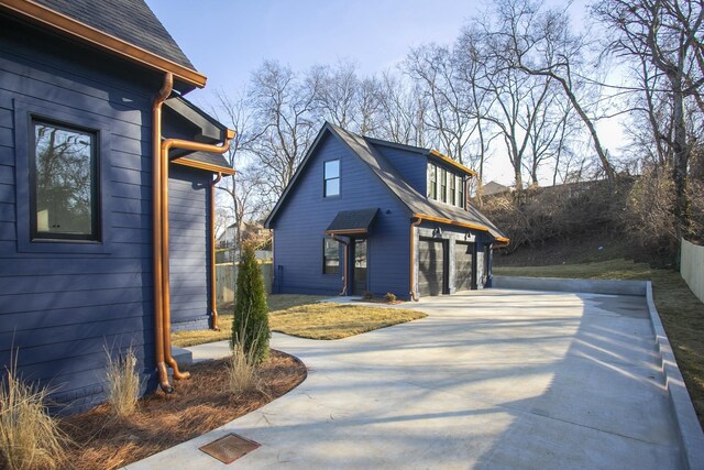 view of property exterior with a garage, concrete driveway, roof with shingles, and fence