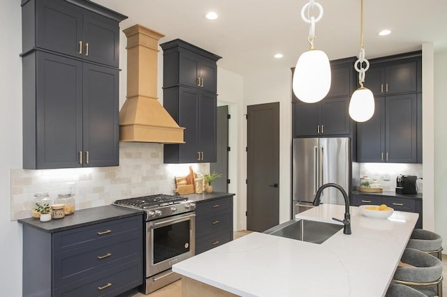 kitchen with dark countertops, an island with sink, custom range hood, stainless steel appliances, and a sink