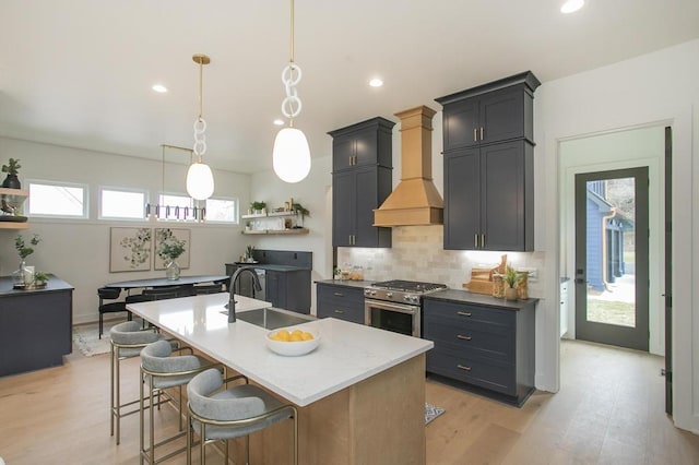 kitchen featuring a center island with sink, decorative light fixtures, high end stainless steel range, premium range hood, and a sink