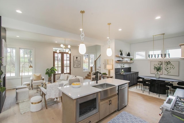 kitchen featuring open floor plan, light countertops, appliances with stainless steel finishes, an island with sink, and decorative light fixtures