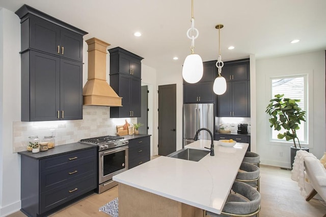 kitchen with pendant lighting, stainless steel appliances, a sink, an island with sink, and dark cabinetry