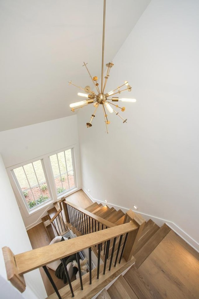 staircase with baseboards, a high ceiling, a chandelier, and wood finished floors