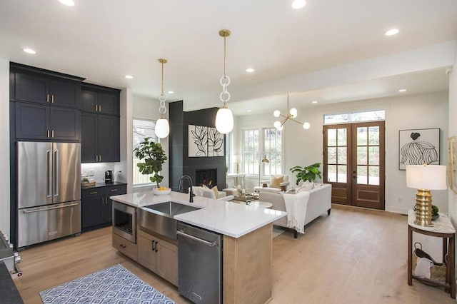 kitchen featuring pendant lighting, stainless steel appliances, light countertops, open floor plan, and an island with sink