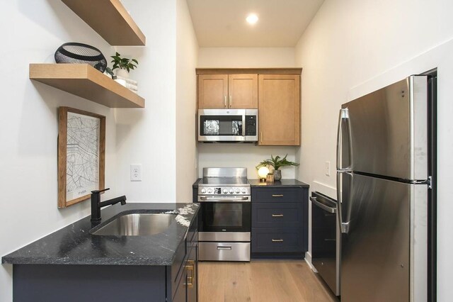 kitchen featuring stainless steel appliances, a sink, light wood-style floors, dark stone counters, and open shelves