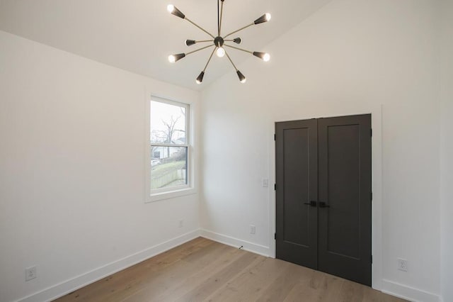 unfurnished bedroom featuring a chandelier, vaulted ceiling, light wood-style flooring, and baseboards