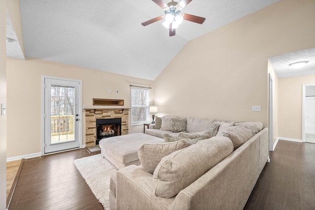 living room with dark hardwood / wood-style flooring, a stone fireplace, vaulted ceiling, and a healthy amount of sunlight