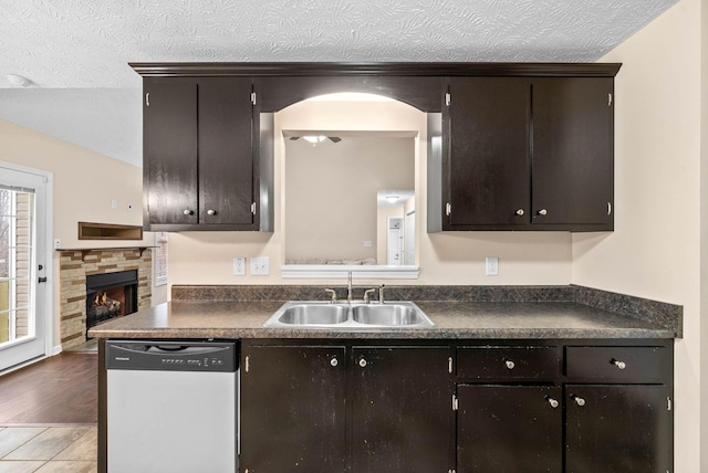 kitchen featuring sink, dark brown cabinets, a fireplace, a textured ceiling, and stainless steel dishwasher