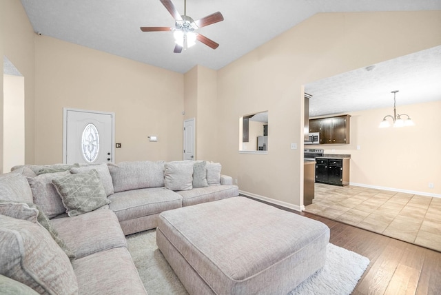 living room featuring high vaulted ceiling, ceiling fan with notable chandelier, and light wood-type flooring